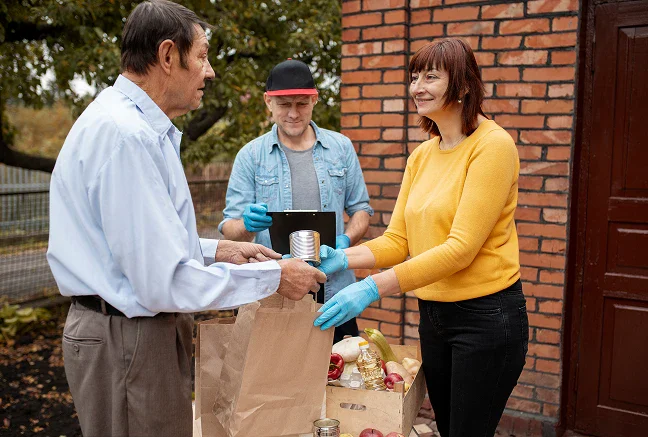Volunteers handing food donations to an older man outside a home