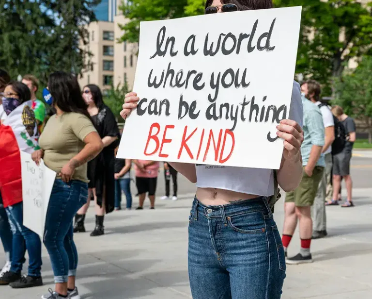 Person holding a sign that says be kind during a public gathering