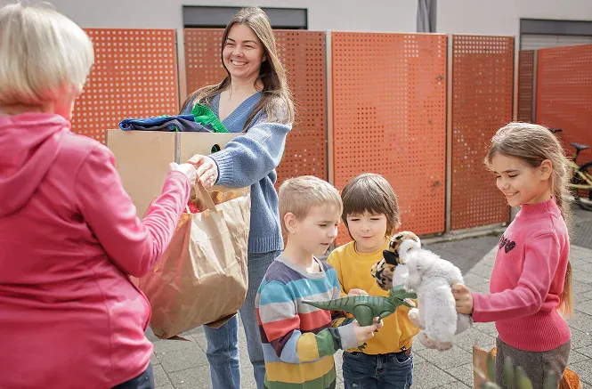 Woman giving a bag of donated items to children while they receive toys and supplies outdoors